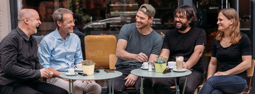 Die 5 Gründer der Coya AG Berlin sitzen lachend an einem Tisch