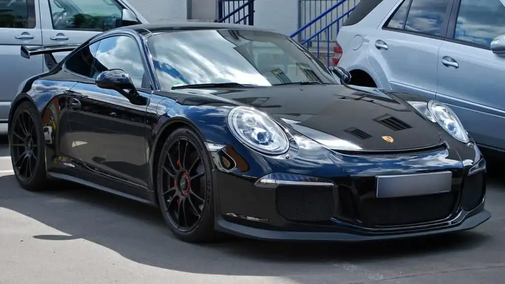 chwarzer Porsche 911 Carrera 2 GTS (997-2) mit sportlichem Design, geparkt auf einem Parkplatz zwischen anderen Fahrzeugen.