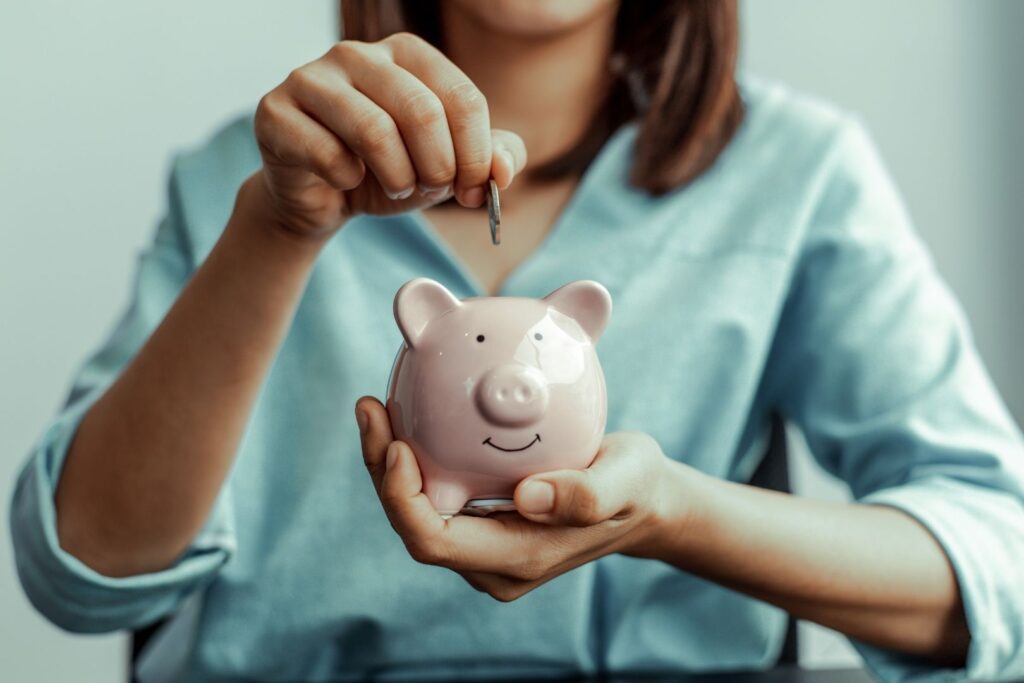 Frau hält Sparschwein und steckt Münze ein – Symbolbild für Beitragspause oder Stundung bei finanziellen Engpässen