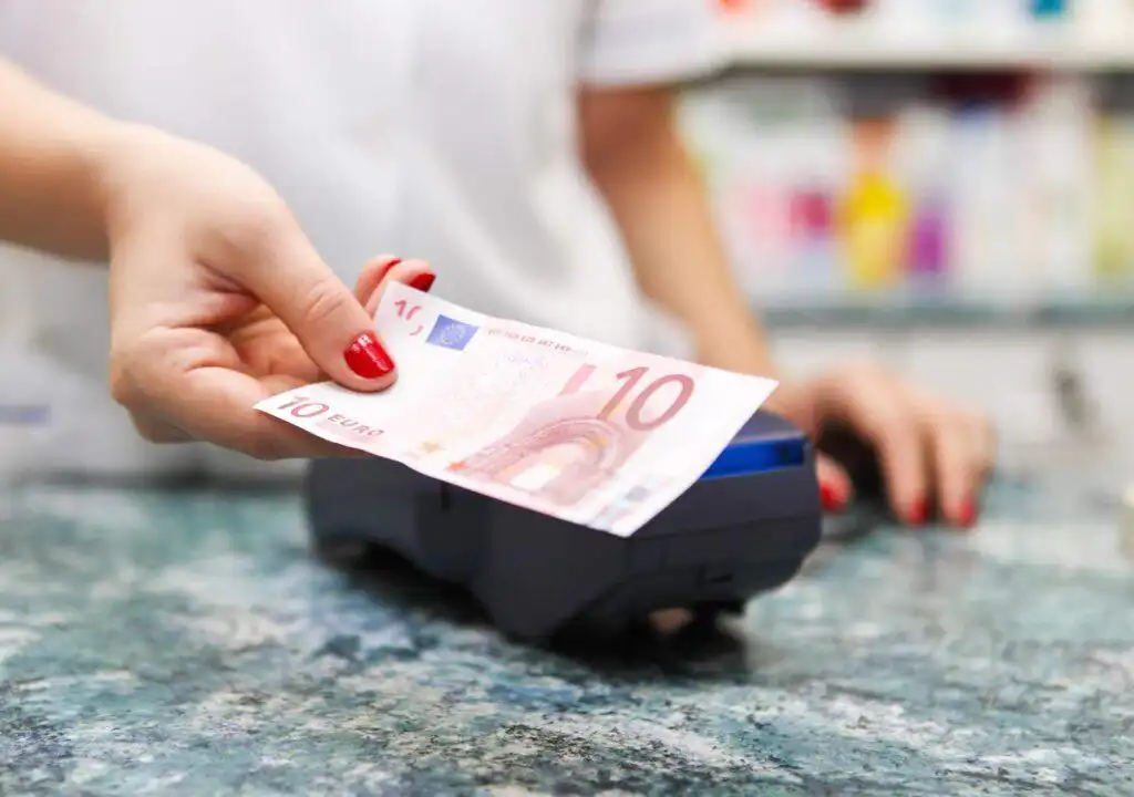 Bezahlung mit einem 10-Euro-Schein an einer Kasse als Symbol für Beiträge und Kosten der privaten Krankenversicherung.