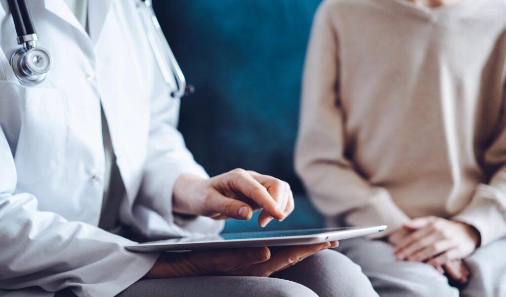 Arzt berät eine Patientin mithilfe eines Tablets als Symbol für Gesundheitsprüfung und Voraussetzungen für die private Krankenversicherung.