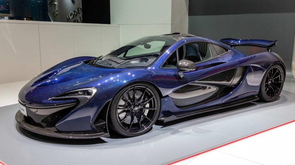 Blauer McLaren P1 in schräger Seiten- und Frontansicht auf einer Automesse mit sichtbaren Carbon-Elementen und Heckflügel.